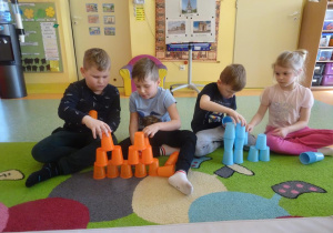 Dzieci układają z kolorowych kubków plastikowych dwie wieże.